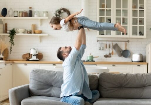 Father holding lifting cheerful daughter having fun at home Happy funny little kid girl flying in fathers arms family having fun in modern studio apartments, loving single daddy holding lifting cheerful pre-school daughter playing plane enjoy playtime at home